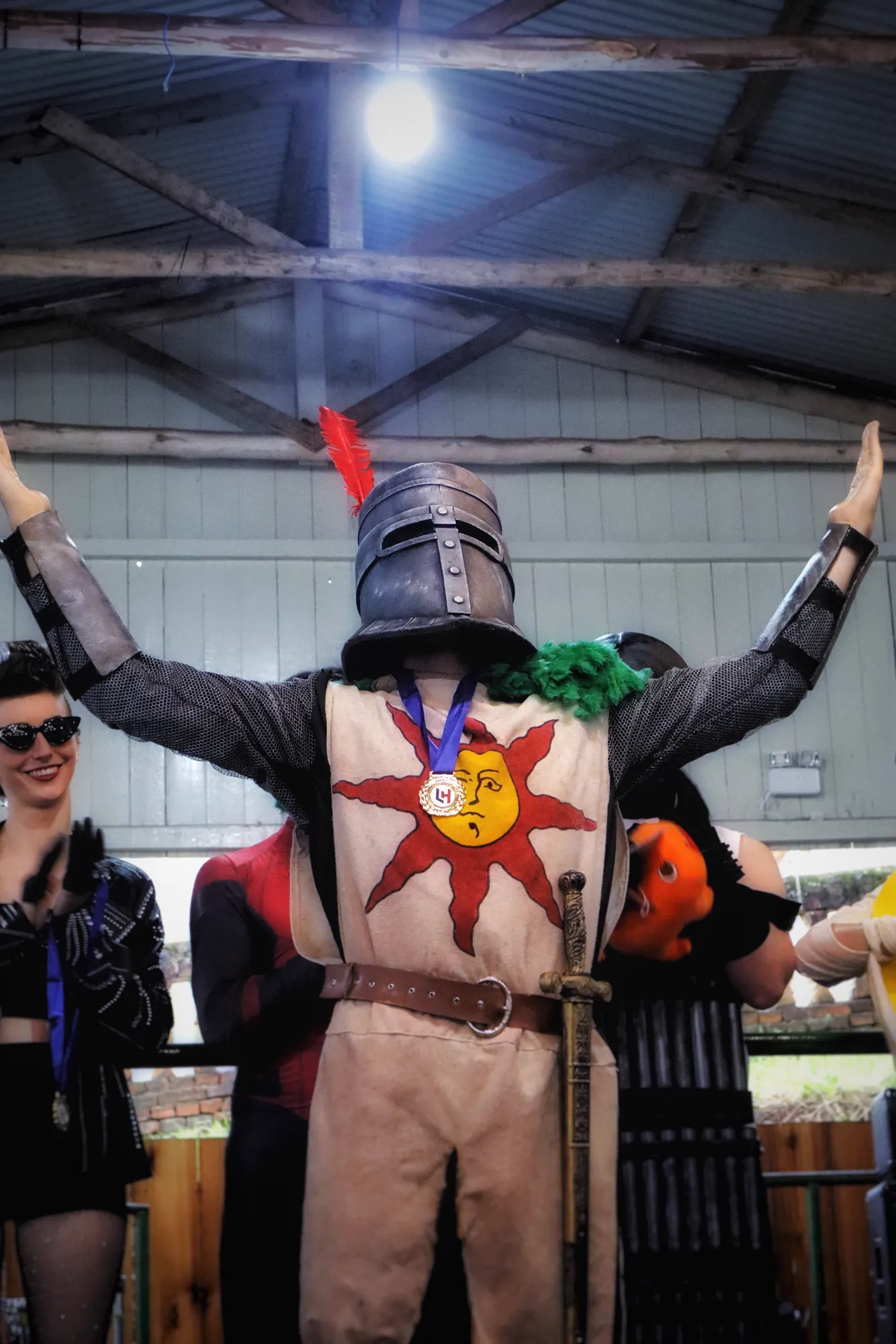 Cosplayer de cavaleiro com os braços erguidos no palco